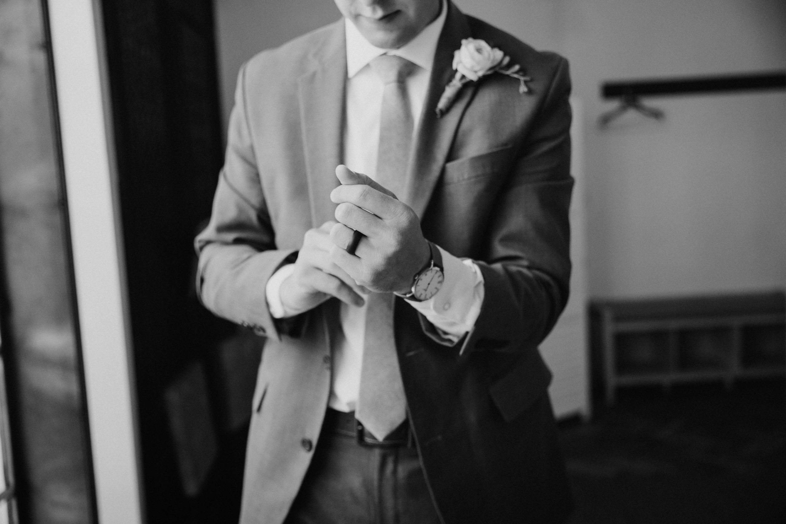 Black and white image of groom adjusting his cufflinks while getting ready on his wedding day taken by Phoenix wedding photographer, Kaylie Miller.