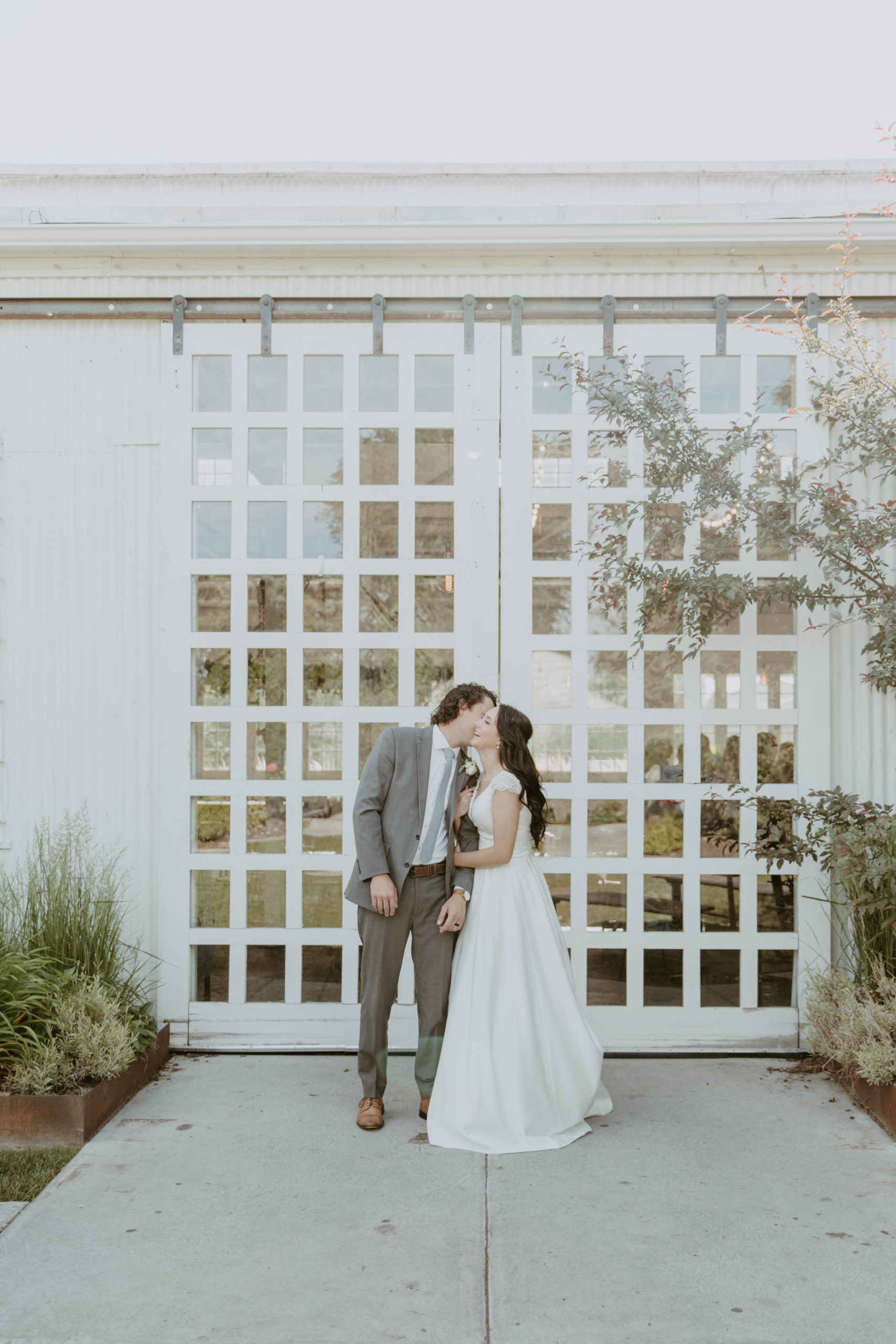 Bride and groom holding hands while kissing during bridal portraits outside the White Shanty venue in Provo, Utah with white barn doors in the background.