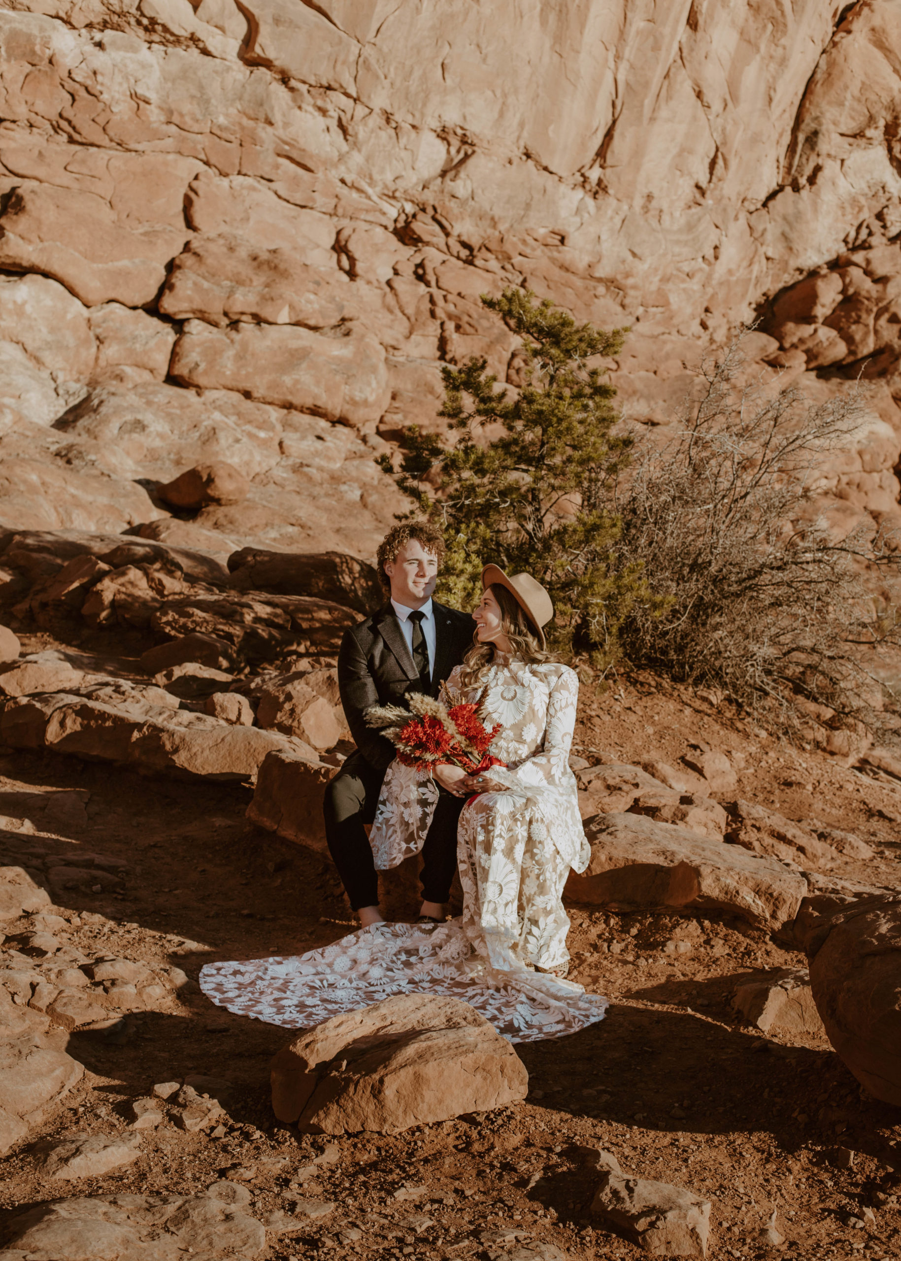 Married couple sitting on the red rocks at Arches National Park looking at each other in Utah.