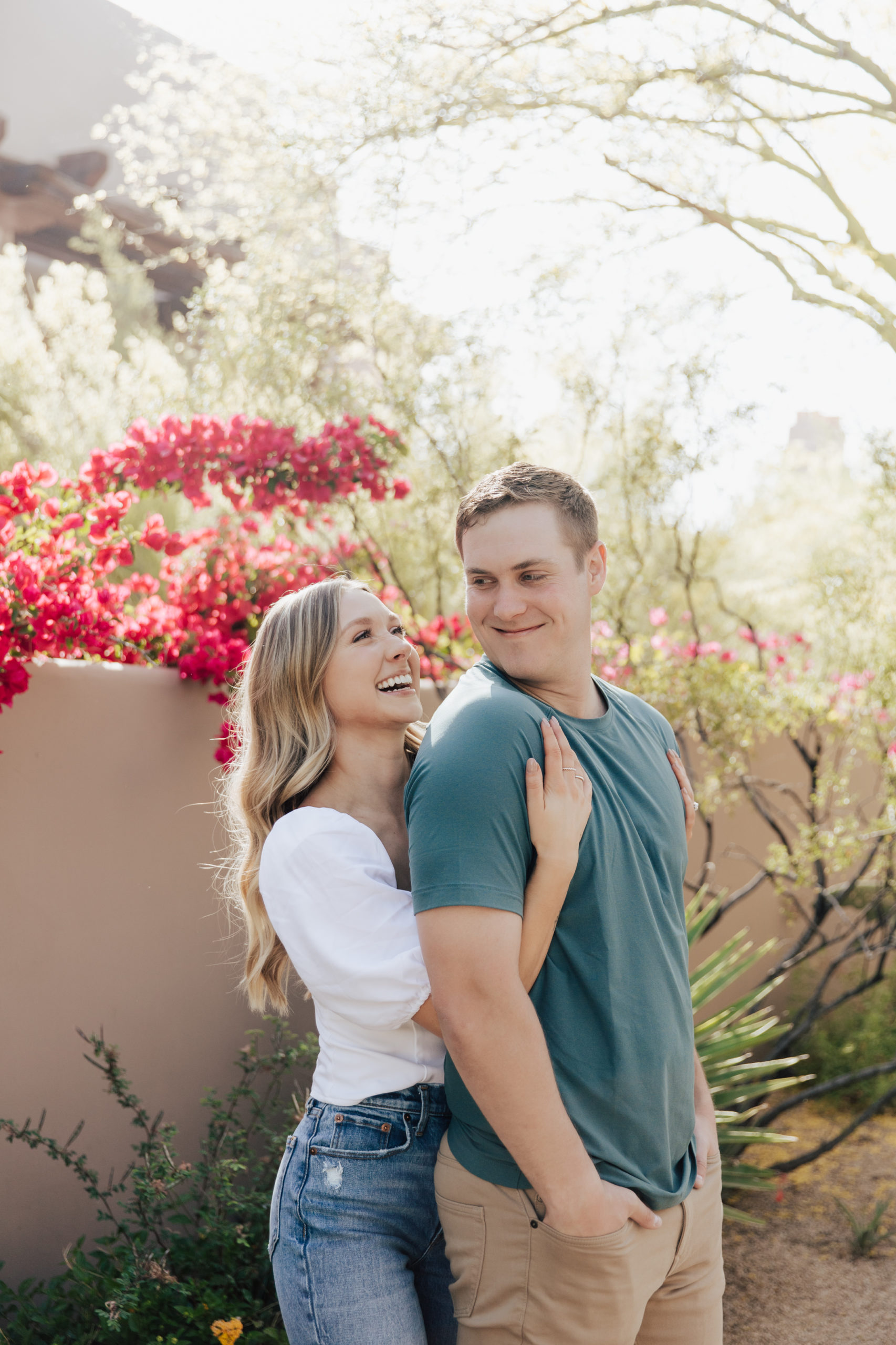 Couple hugging and laughing in front of pink spring flowers at the Four Seasons Resort in Scottsdale.